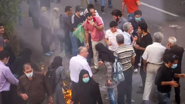 Des manifestants se rassemblent lors de la manifestation de 2009, certains se soufflant de la fumée dans les yeux pour atténuer l'effet des gaz lacrymogènes.