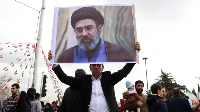 Un Iranien, vêtu d'une veste de costume noire et d'une chemise blanche, tient une photo de Mojtaba Khamenei, lors des célébrations du 47e anniversaire de la révolution islamique à Téhéran, le 11 février 2026.